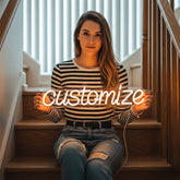 Woman sitting on stairs holding a neon sign with 'customize' text