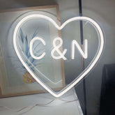 Neon heart-shaped sign with 'C&N' inside, placed on a surface with a blurred background.