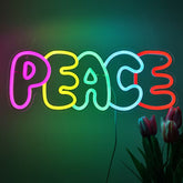 Neon sign spelling 'PEACE' with colorful letters on a dark background, accompanied by flowers.