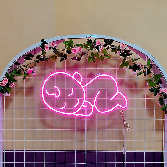 Neon sign of a baby lying on its back with pink outline, placed against a tiled wall with floral decorations.