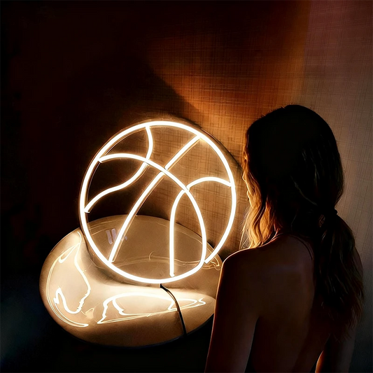 Person standing next to a glowing basketball-shaped light fixture in a dark room.