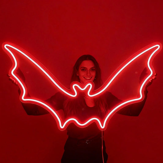 A smilling woman holding a red color neon sign shaped like a bat in a dark background.
