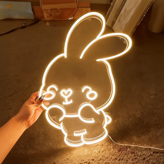 Neon warm white bunny light shaped like a cartoon character held by a hand on a dark surface.