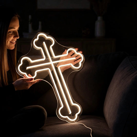 Person holding a warm white neon cross-shaped light in a dark setting