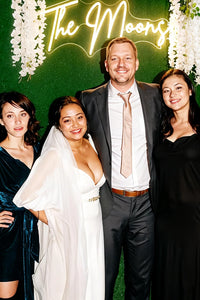 Group of four people posing in front of a green backdrop with 'The Moons' neon sign.