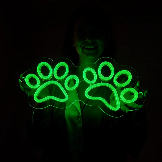 A woman holding a green neon sign with paw designs in a dark setting