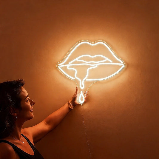 Woman holding a neon warm white sign shaped like lips against a wall.
