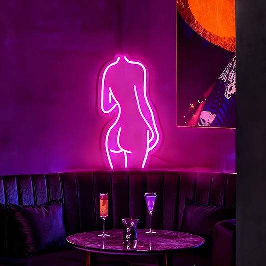 Neon sign of a woman's silhouette on a dark wall with a table and drinks in the foreground.