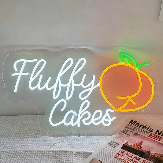 Neon sign with 'Fluffy Cakes' and a peach graphic on a white surface.