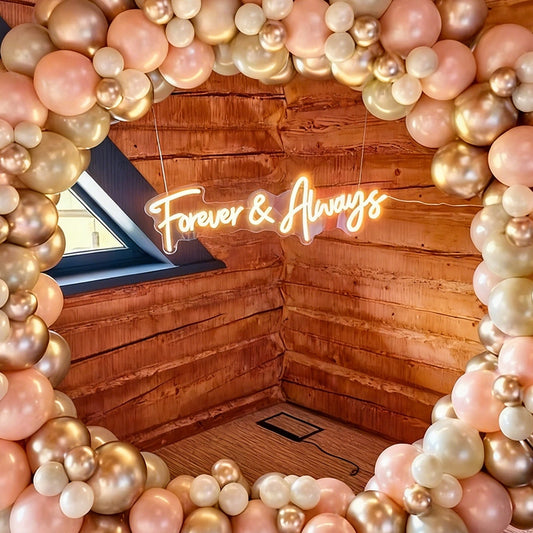 Neon sign reading 'Forever & Always' surrounded by pink and gold balloons in a wooden cabin.