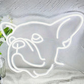 Neon light shaped like a dog on a textured surface with plants.