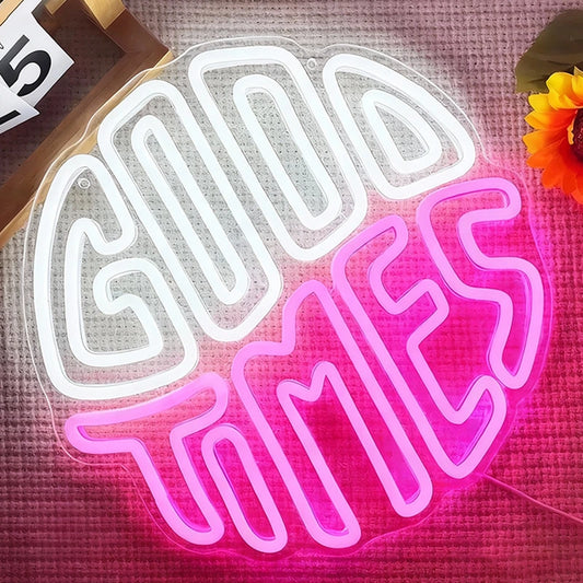 Neon sign with 'Good Times' in white and pink on a textured surface with a sunflower.