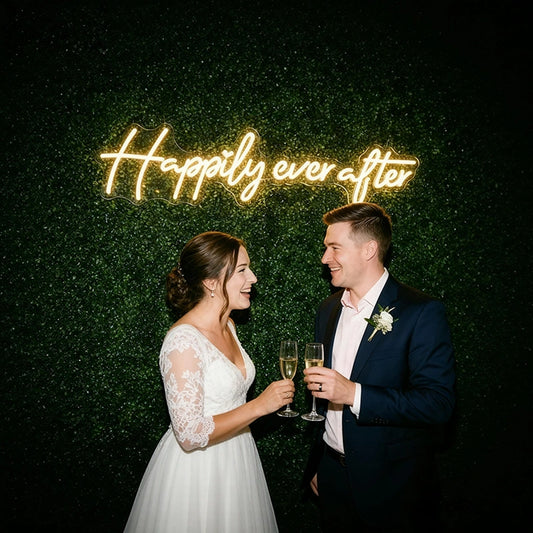 Couple in wedding attire standing in front of a 'Happily ever after' neon sign.