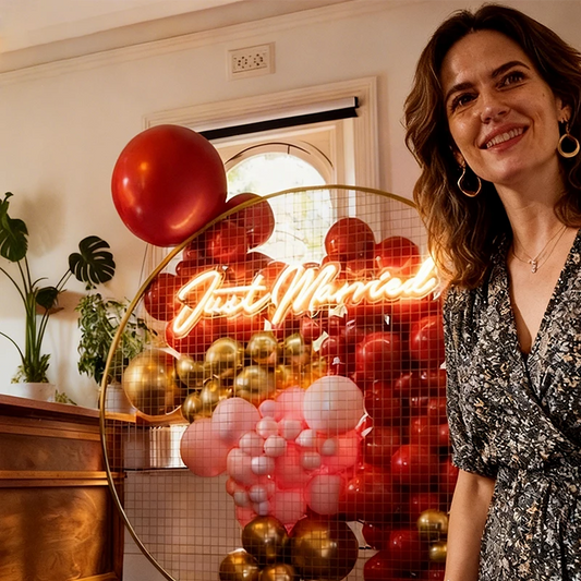 Woman standing in front of a decorative wall with balloons and a "just married" neon sign.