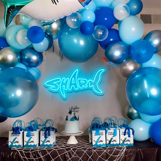 Decorative arch with blue balloons and a neon 'Shark' sign at a party.