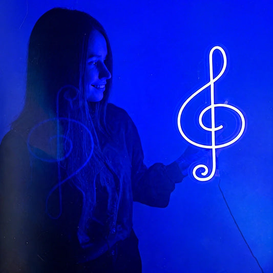 Person holding a neon treble clef sign against a blue background