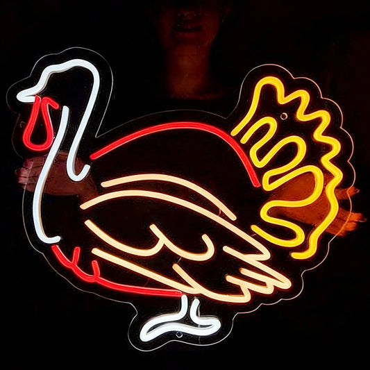 A neon-style turkey sign glowing against a dark background, with white, warm white, red, and lemon yellow illuminated tubing forming the bird's outline and body details.