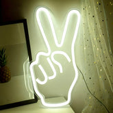 Neon light shaped like a hand making a peace sign on a table with a curtain in the background.
