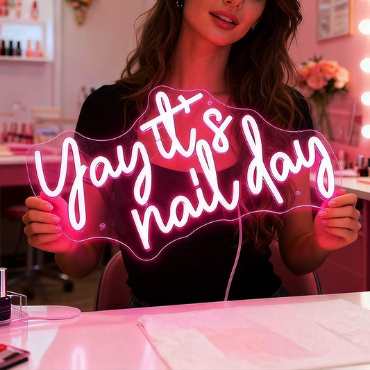 Woman holding a neon sign that says 'Yay it's nail day' in a nail salon.