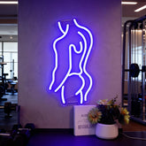 Neon sign of a stylized figure on a wall in an indoor setting with gym equipment.