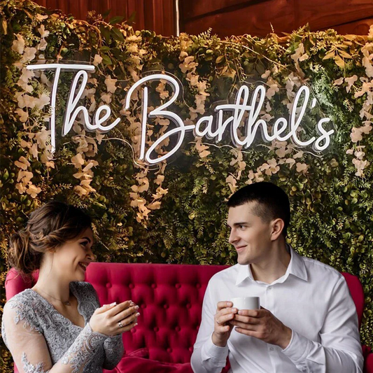 Couple sitting on a red couch with a decorative wall and 'The Barthel's' sign.