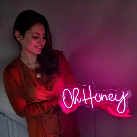 Woman holding a neon sign with 'Oh Honey' text against a dark background