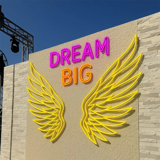 Neon sign with 'Dream Big' and yellow wings on a building facade.