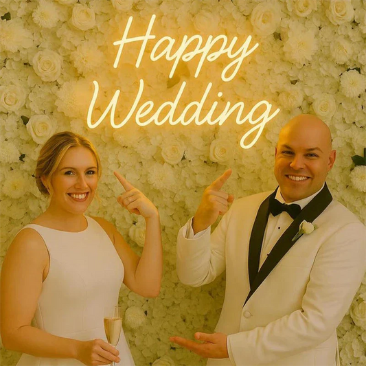 Man and woman in formal attire pointing at a 'Happy Wedding' sign with a floral background