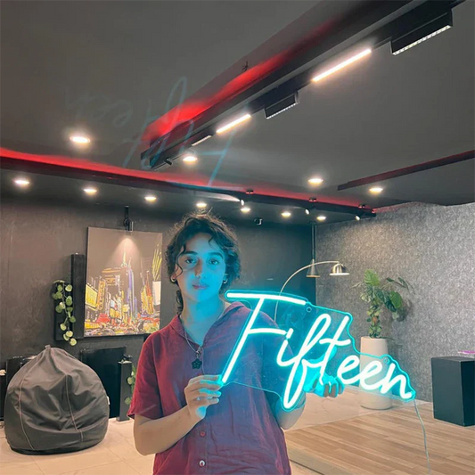 Person holding a neon sign with 'Fifteen' in a modern room with decor elements.