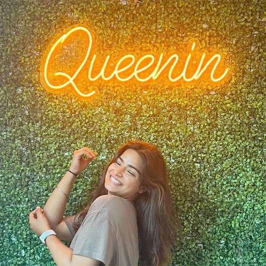 Woman lying on grass with 'Queenin' neon sign in the background