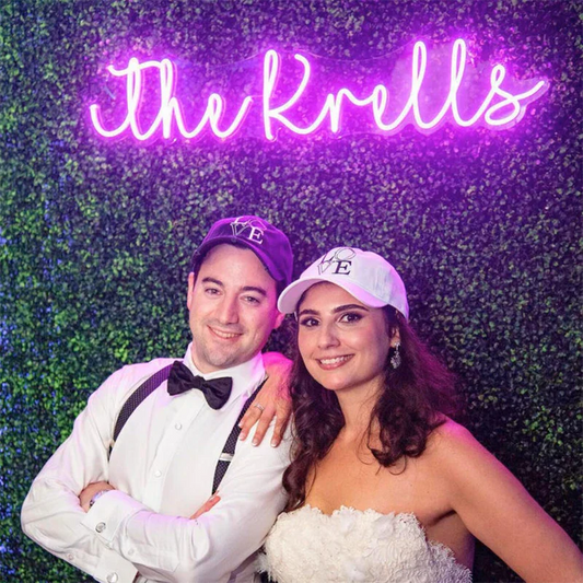 Two people in formal attire standing in front of a neon sign with 'the Krells' on a green leafy background.