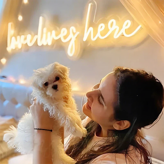 Woman holding a small white dog with a 'love lives here' neon sign in the background