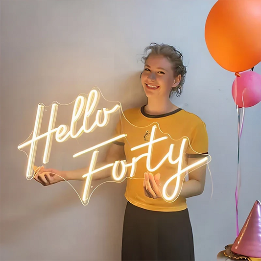 Person holding a 'Hello Forty' neon sign with balloons in the background