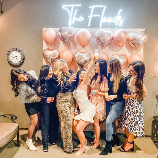 Group of women posing in front of a balloon arch with 'The Floods' sign in the background.