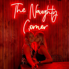 Two young girls standing together with a red neon sign behind that reads 'The Naught Corner' .