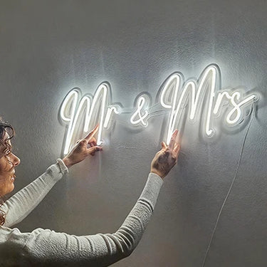 Person interacting with a neon 'Mr & Mrs' sign on a wall