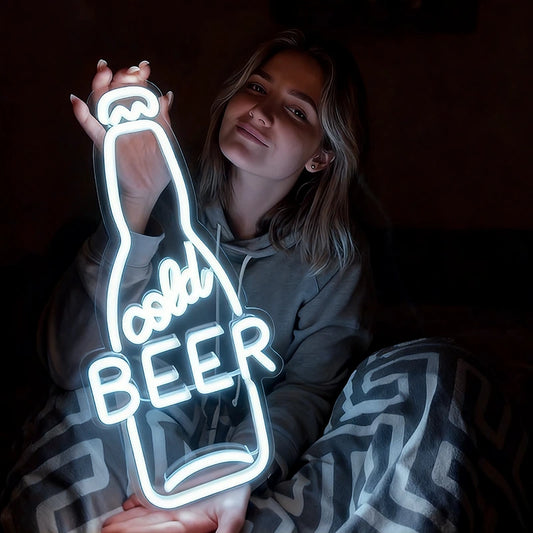 Person holding a neon white sign shaped like a beer bottle with the word 'cold BEER' inside.