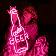 Person holding a neon hot pink sign shaped like a beer bottle with the word 'cold BEER' inside.