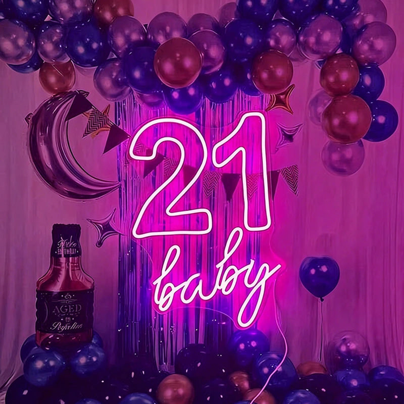 Neon sign with '21 baby' surrounded by balloons and a bottle of alcohol on a pink background