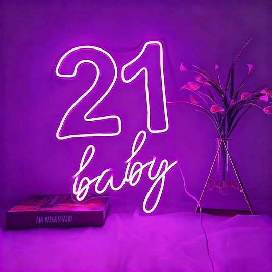 Neon sign with '21 baby' on a purple background with a book and plant.