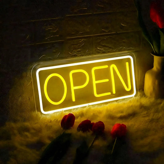 Neon 'OPEN' sign illuminated in a dimly lit setting with flowers around.