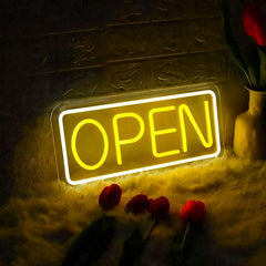 Neon 'OPEN' sign illuminated in a dimly lit setting with flowers around.