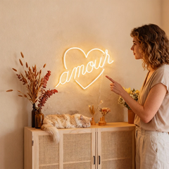 Woman pointing at a neon sign with the word 'amour' in a warm, indoor setting.