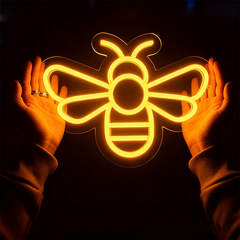 Neon bee light held between two hands against a dark background