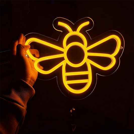Neon bee-shaped light held by a hand against a dark background