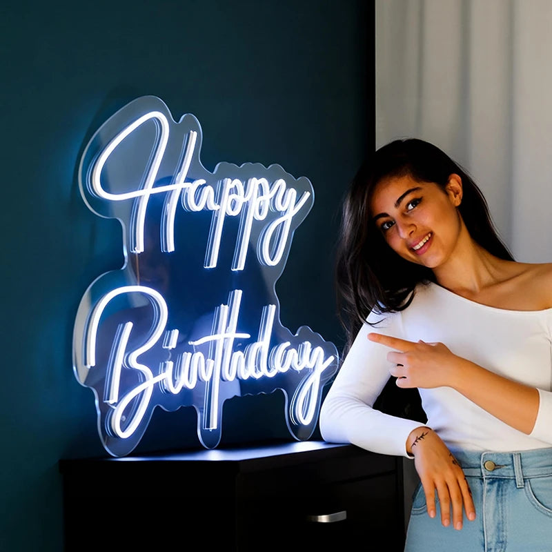 Woman pointing at a 'Happy Birthday' neon sign.