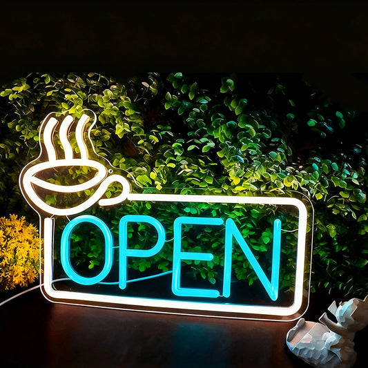 Neon sign with coffee cup icon and 'OPEN' text in front of green foliage