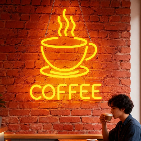 Neon sign of a coffee cup with steam and 'COFFEE' text against a brick wall, with a person drinking coffee in the foreground.