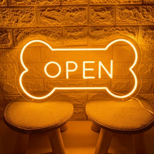 Neon 'OPEN' sign shaped like a bone on a textured wall with stools.