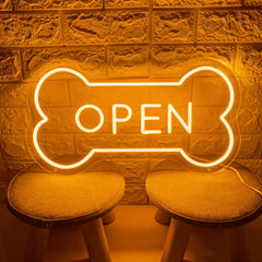 Neon 'OPEN' sign shaped like a bone on a textured wall with stools.